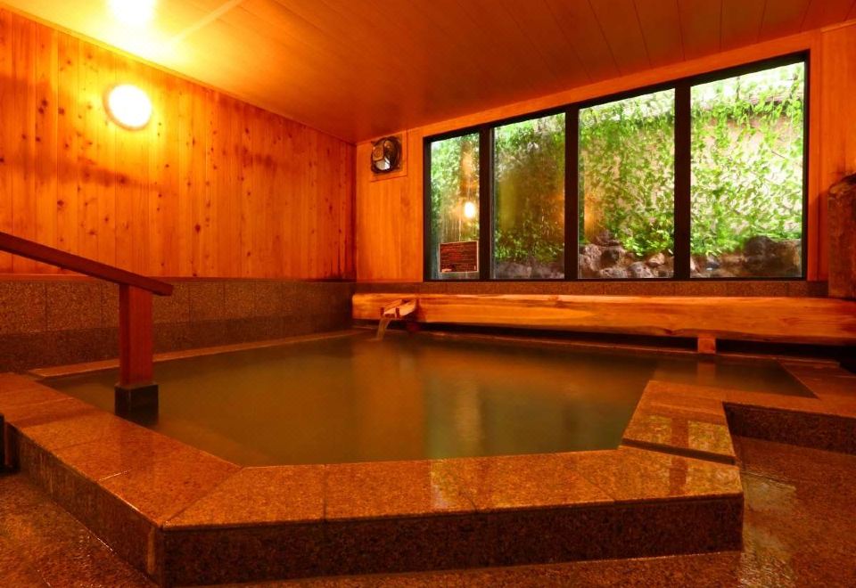 A stone-edged indoor bath beneath wooden walls and a garden window.