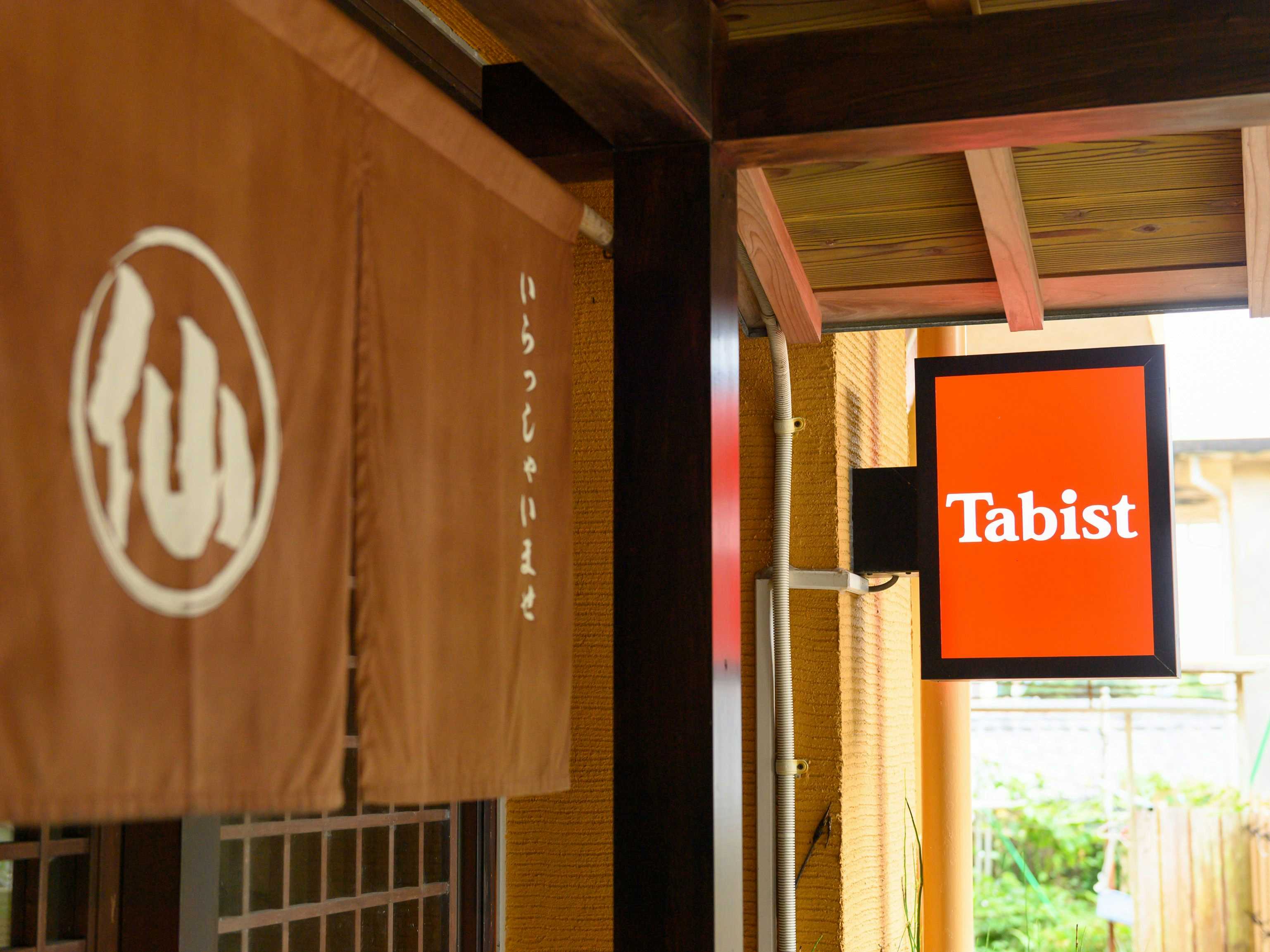 Fish Inn Marusen with a brown noren displaying the inn emblem beside a red sign.