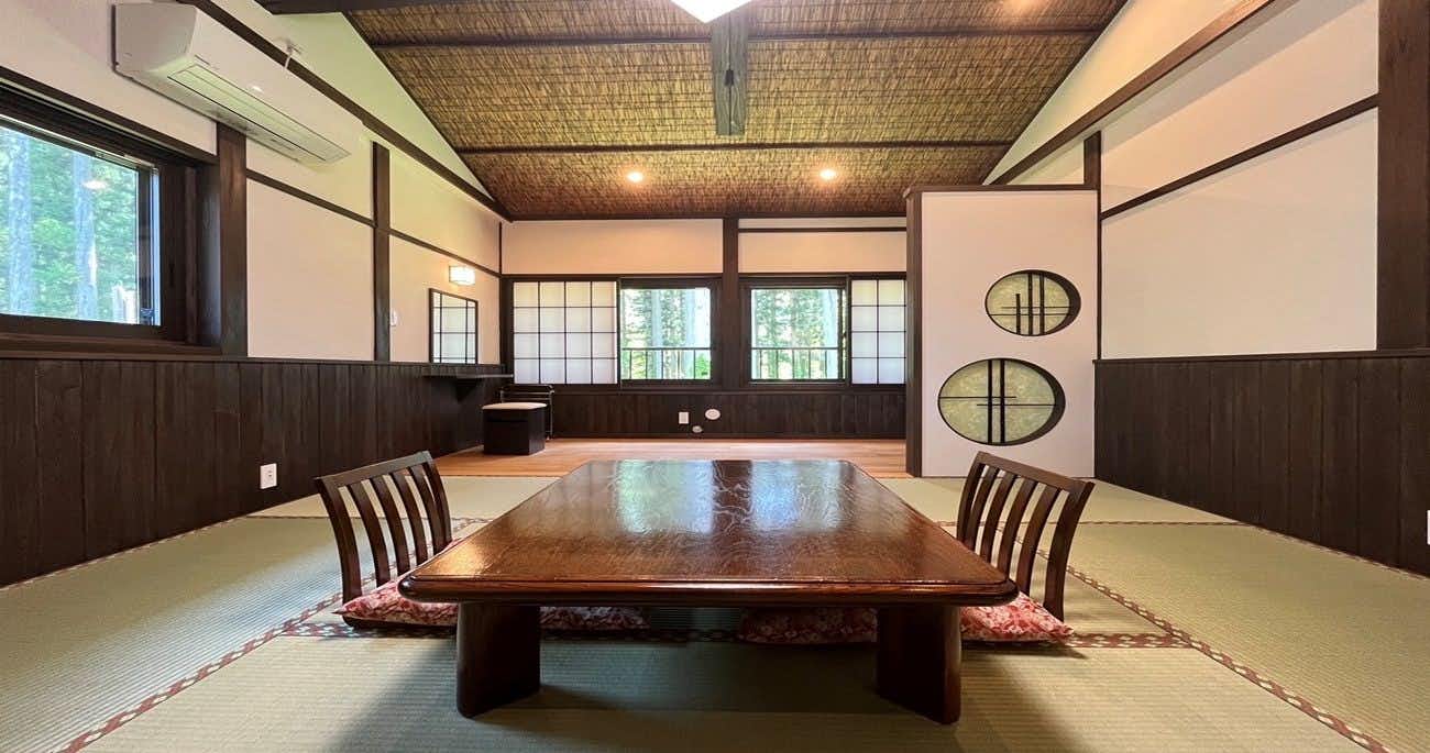 Oyado Yunosato Interior dining room with dark wooden table, cushioned chairs, tatami matting, exposed wooden beams, and grid-patterned windows