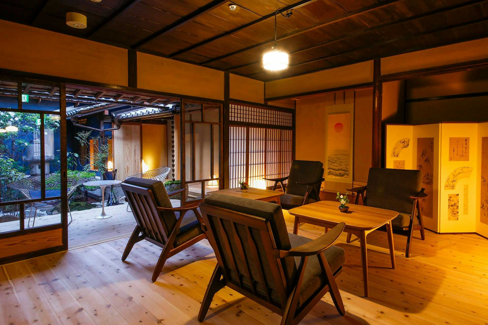 Kariya Ryokan Q with this scene, where low timber chairs and tables furnish a warm garden-facing lounge.