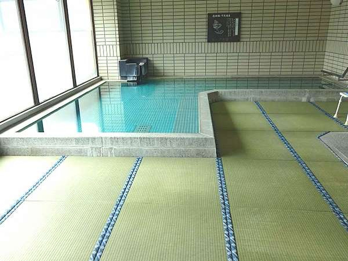 A small indoor bath surrounded by tatami-style flooring.